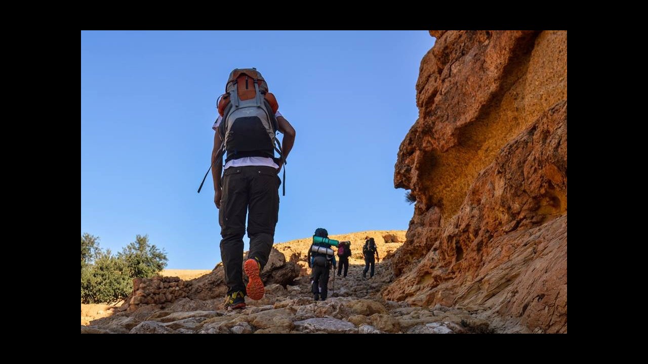 Trekkers ascend the rocky, ancient path towards the village of Chenini, exploring the stunning landscapes of the Dahar region